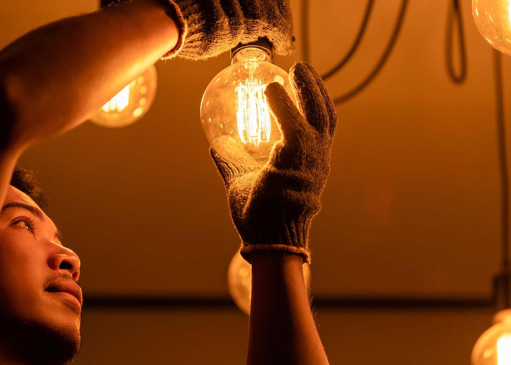 A person in gloves changing a glowing light bulb